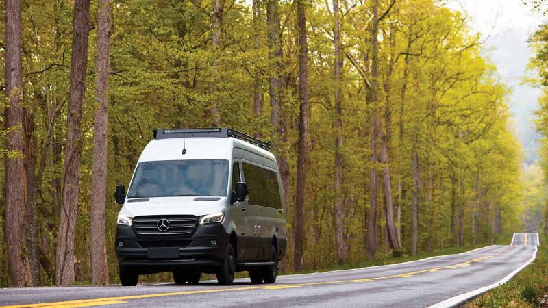 Silver Class B Airstream driving on a forest road