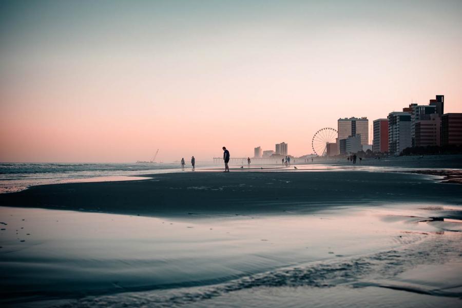 Sunset on Myrtle Beach, with people on the shoreline and high rise buildings in the distance