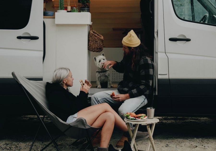 Small white dog sitting with a man and a woman at the edge of a campervan